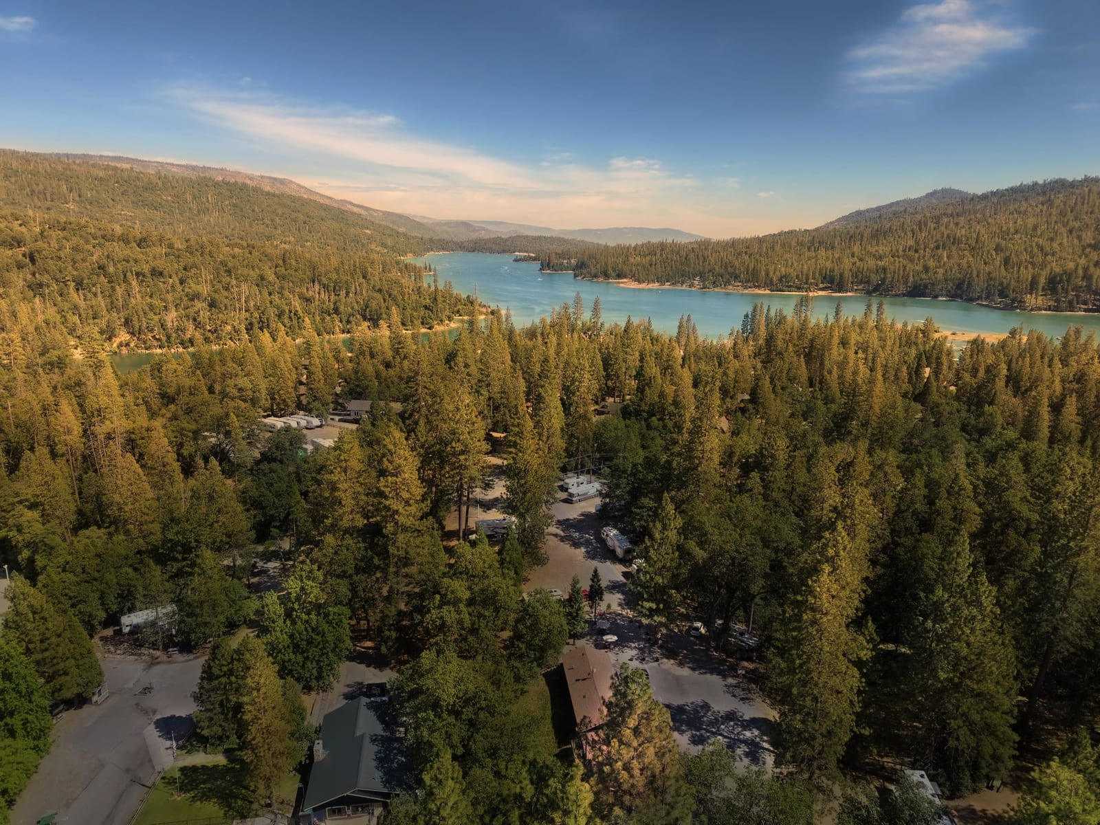 Aerial view of Outdoorsy Yosemite at golden hour, RV sites among the pines with Bass Lake beyond